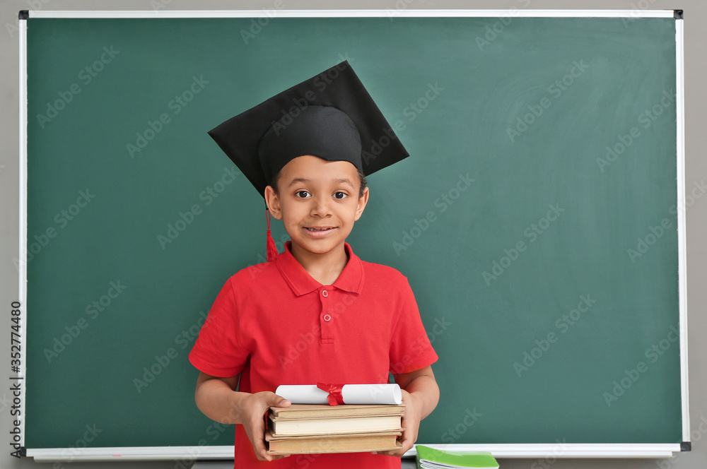 戴着毕业帽的非洲裔小男孩，黑板附近有书和文凭