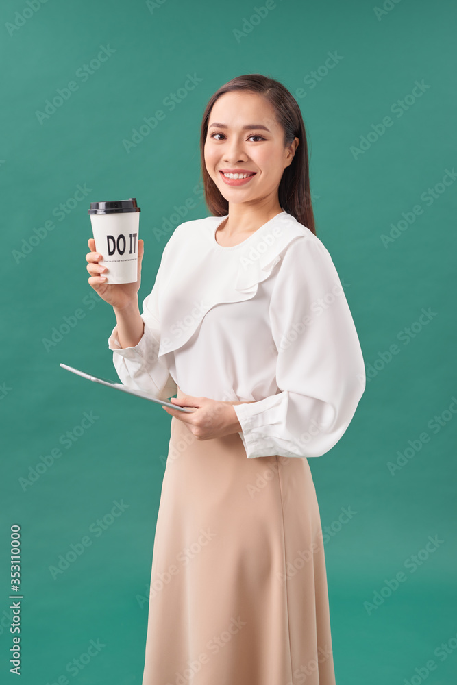 Attractive woman wearing shirt holding tablet and drinking takeaway coffee standing isolated over tu
