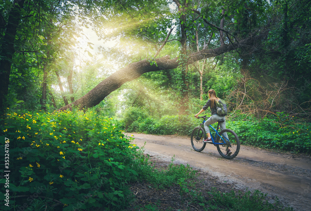 Woman riding a bicycle in forest in spring at sunset. Colorful landscape with sporty girl with backp