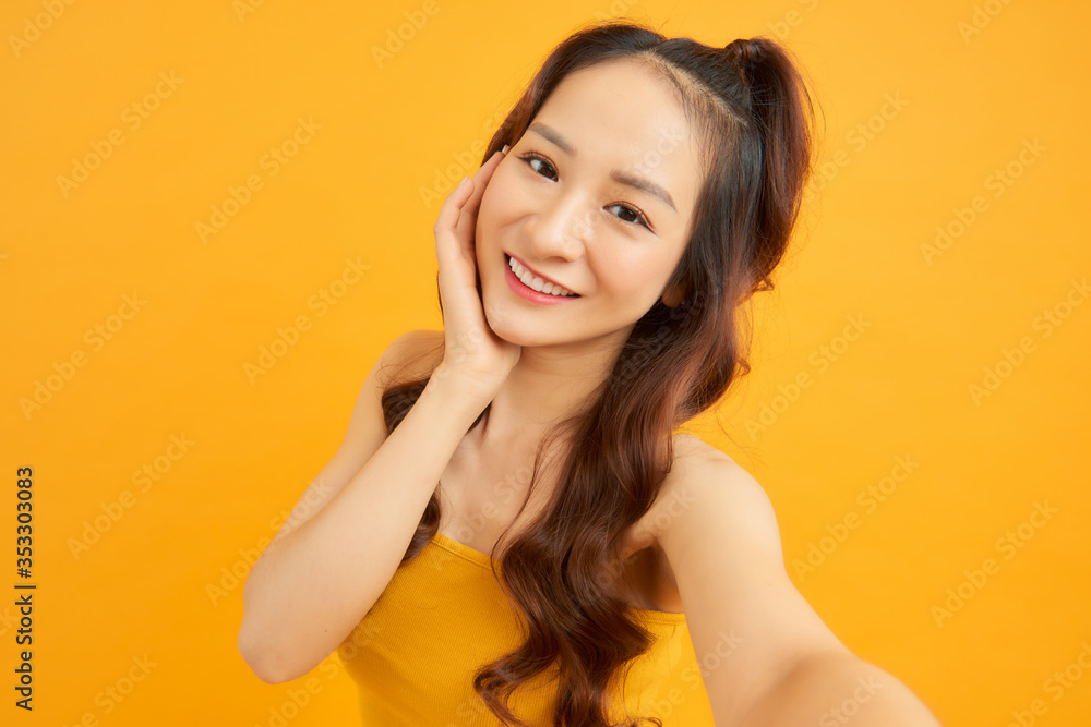 橙色背景下，美丽女孩在相机前自拍的肖像。夏季概念