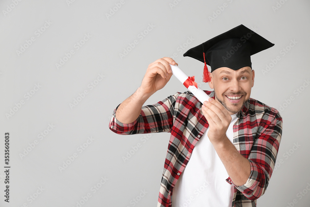 Man in graduation hat and with diploma on grey background
