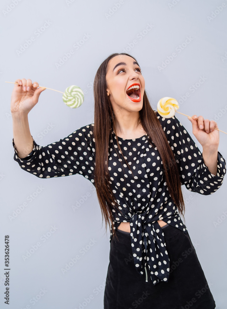 Young beauty in dotted shirt with two lollipops in hands. Cheerful lady with candies over white back