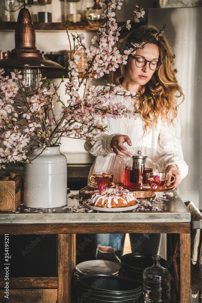 春天或夏天的茶和蛋糕。年轻的金发女人提供玫瑰和杏仁无麸质的bundt c
