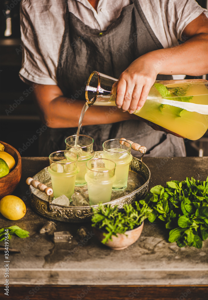 Hands of woman making fresh homemade lemonade over marble kitchen counter. Woman pouring cold lemona
