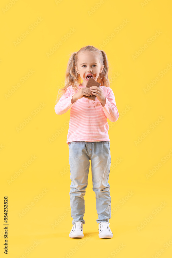 Little girl in dirty clothes eating chocolate on color background