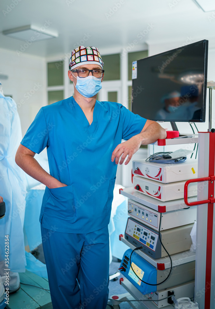 医疗设备附近戴着外科口罩的专业医疗助理肖像。现代医院