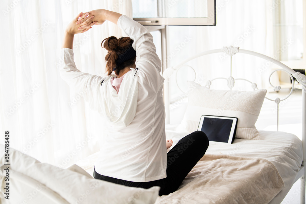 オンラインレッスンを受けてベッドの上でストレッチする女性