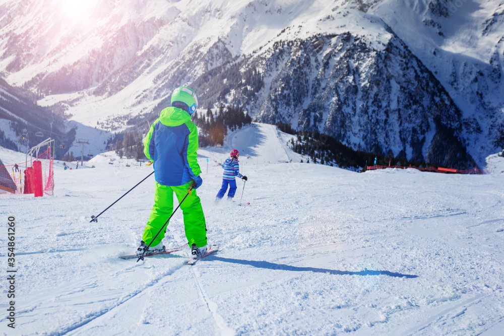 两个10岁的孩子在阿尔卑斯山阳光明媚的日子里沿着斜坡奔跑，从后面看