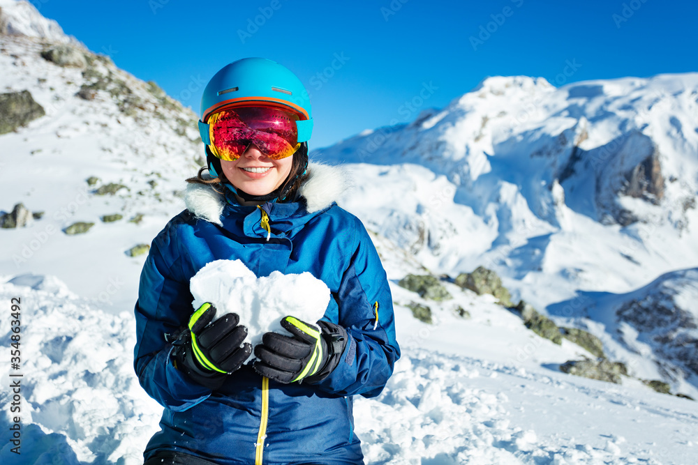 Smiling teenage girl in blue outfit mask and helmet show love concept holding snow heart shape