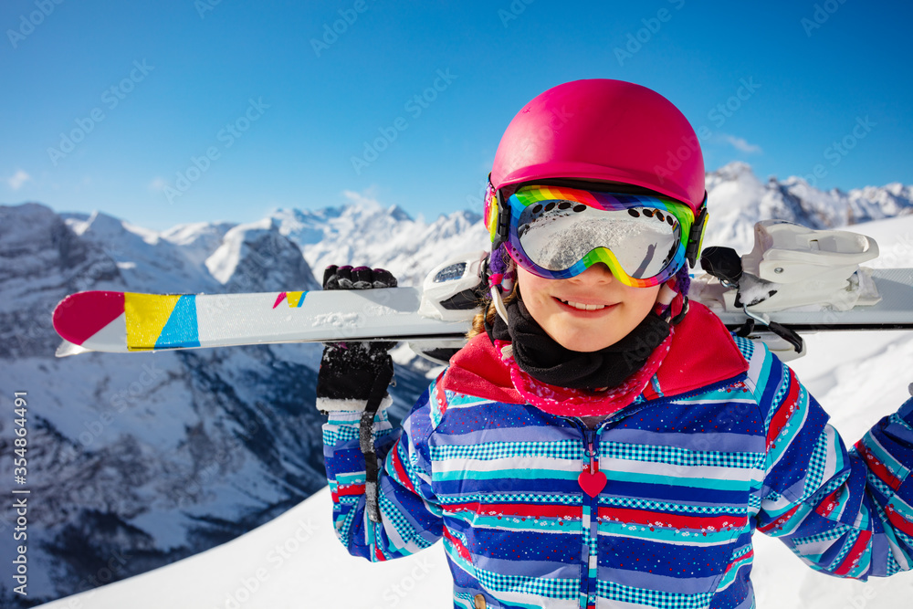 一个女孩的特写头像，她穿着五颜六色的衣服，戴着粉色头盔和彩色眼镜，手里拿着滑雪板。