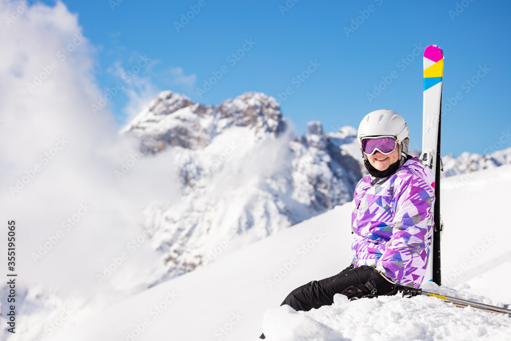穿着滑雪服、戴着头盔和口罩的十几岁女孩坐在山顶的雪地里看的照片来了