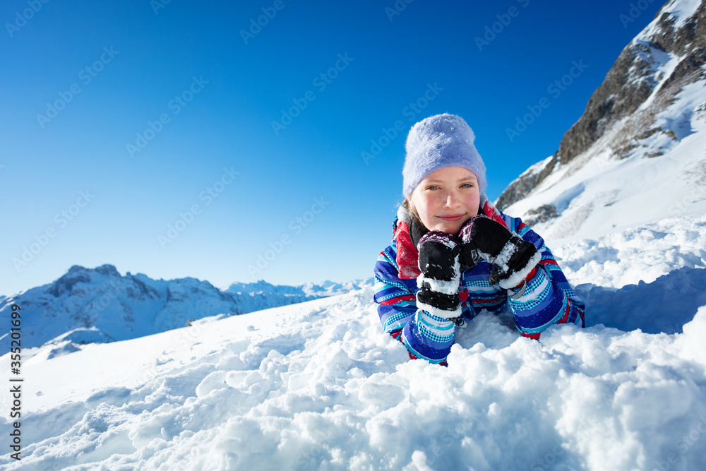 快乐微笑的小女孩躺在雪地里，双手抱头，戴着冬帽微笑