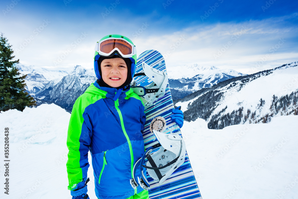一个男孩手拿滑雪板翻越高山全景的正面肖像