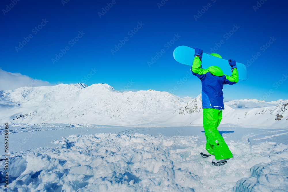 一个男孩的背面肖像，肩上扛着滑雪板，站在山顶的雪地里