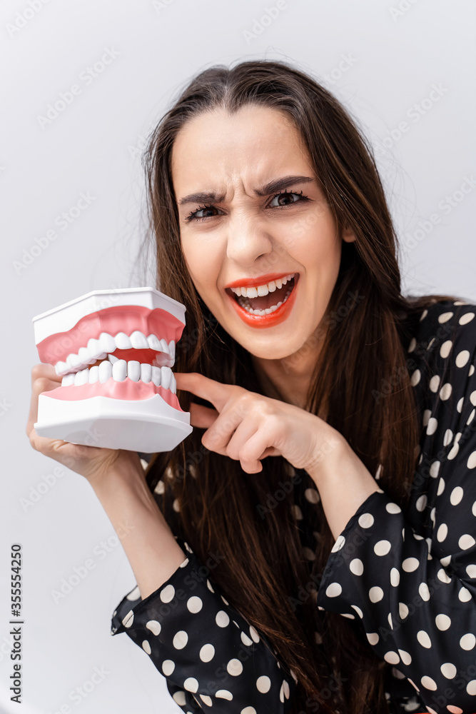 Girl put finger to a dental educational jaw. Plastic jaw bites a girl by a finger. Funny emotions.