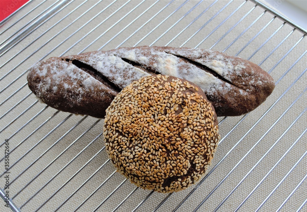 金属网架上的自制黑麦面包：一个芝麻圆面包和一个法式迷你法棍面包