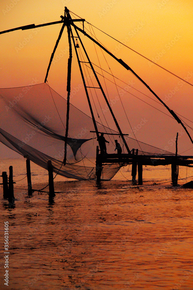 silhouette of fisherman fishing with large net during sunset in cochin - india 