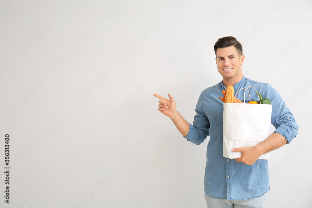 Young man with food in bag showing something on light background