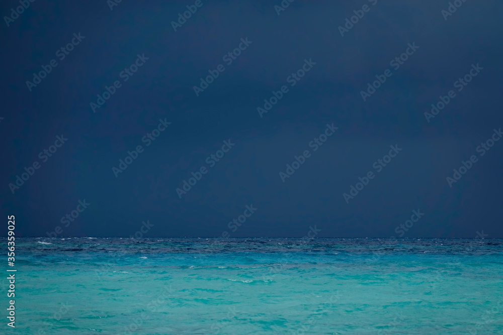 Dark stormy skies gather above the endless turquoise colored ocean in Maldives.