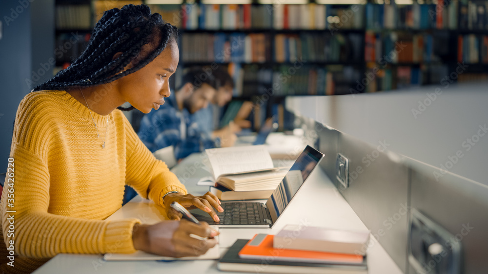 大学图书馆：天才黑人女孩使用笔记本电脑，为论文、论文、冲突研究写笔记