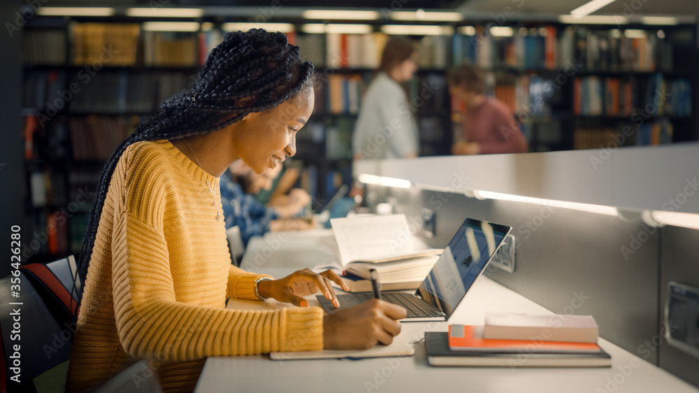 University Library: Gifted Beautiful Black Girl Sitting at the Desk, Uses Laptop, Writes Notes for t