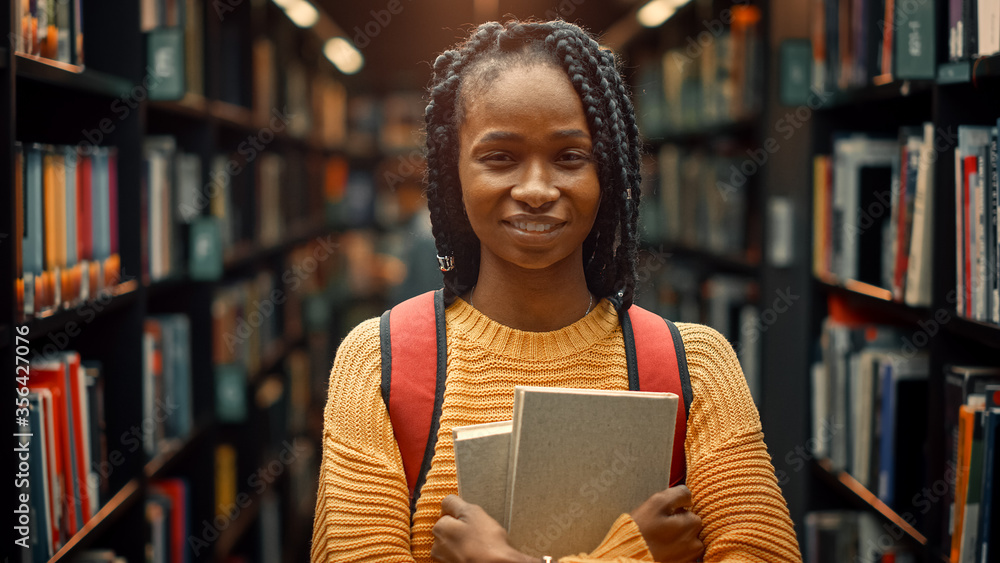 大学图书馆研究：一个聪明漂亮的黑人女孩微笑着拿着研究课本的画像