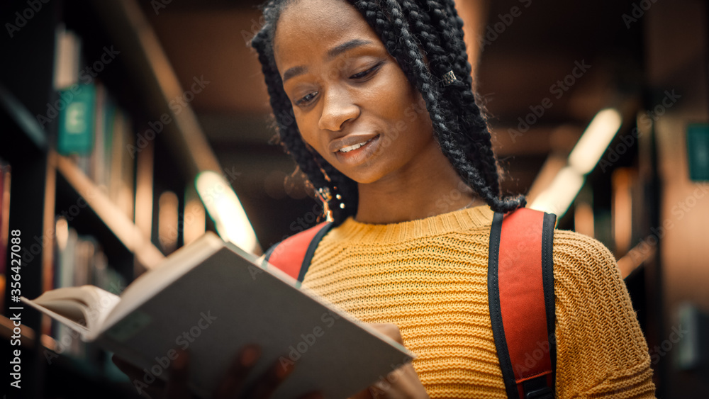 大学图书馆：聪明漂亮的黑人女孩站在书架旁，手里拿着文本B阅读