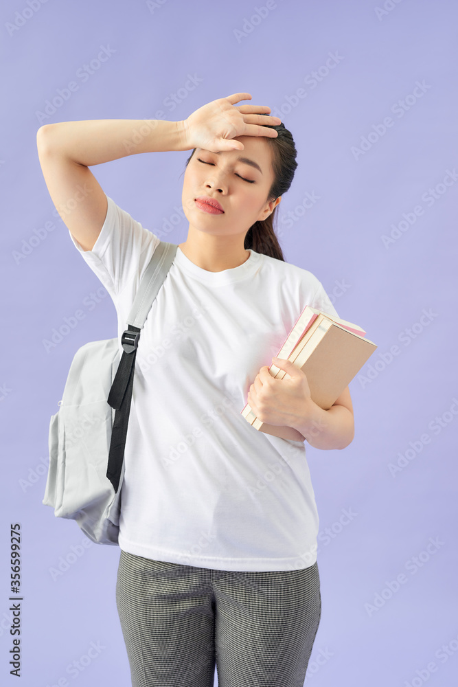 疲惫的年轻女学生，紫色背景背着背包。抱着书闭着眼睛放哈