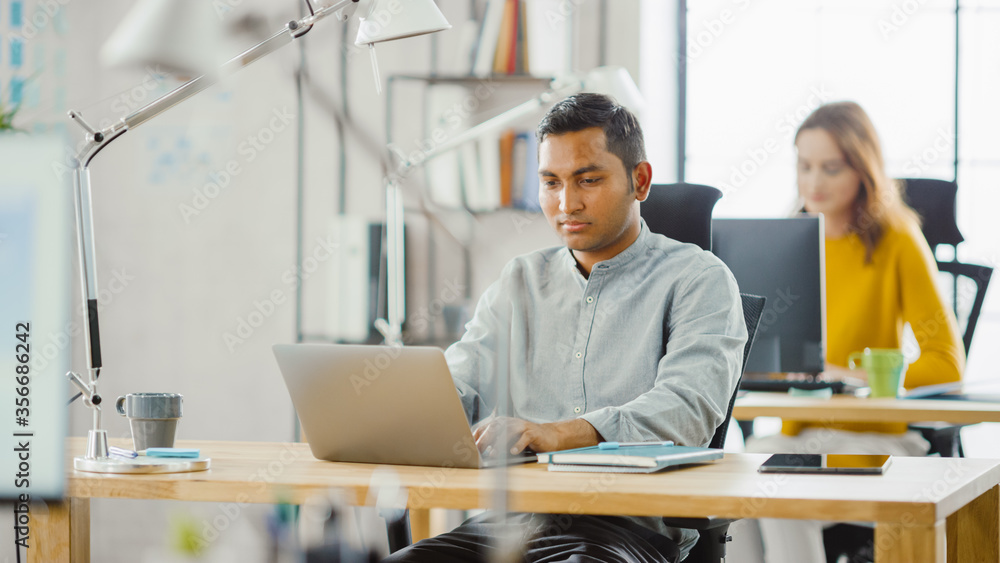聪明英俊的印度信息技术专家坐在办公桌前用笔记本电脑工作。我