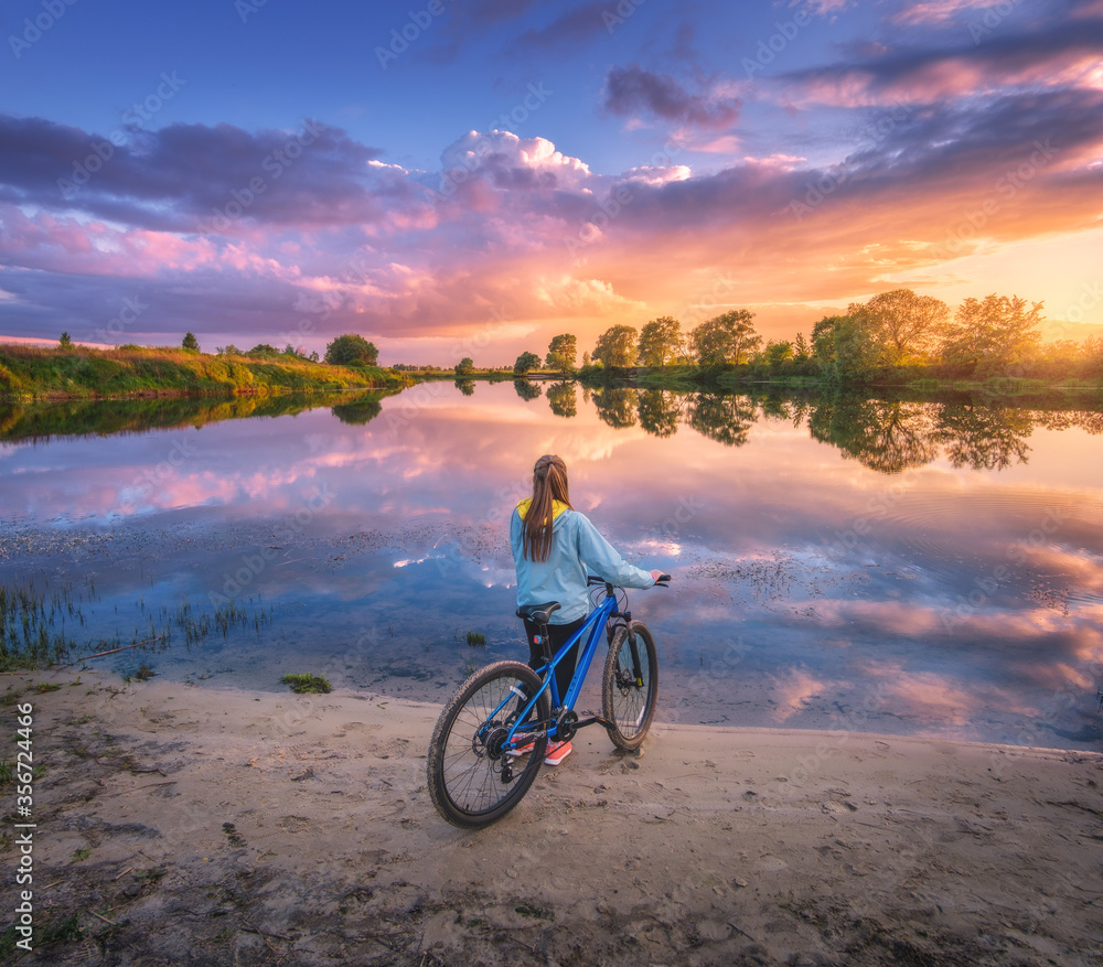 夏天日落时，河边骑自行车的女人。与年轻女孩一起欣赏风景