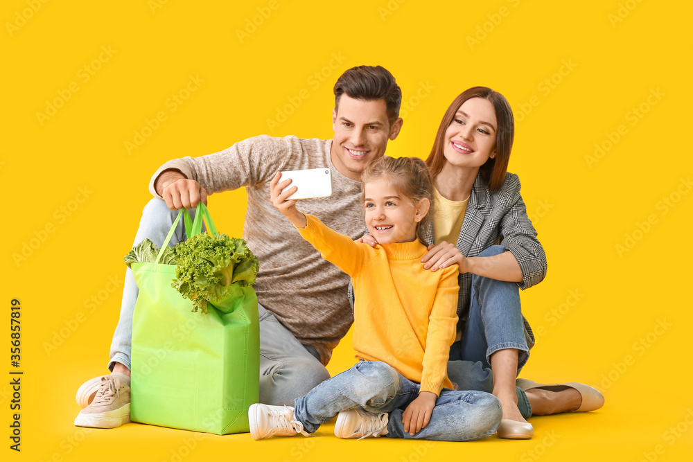 Family with food in bag and mobile phone on color background
