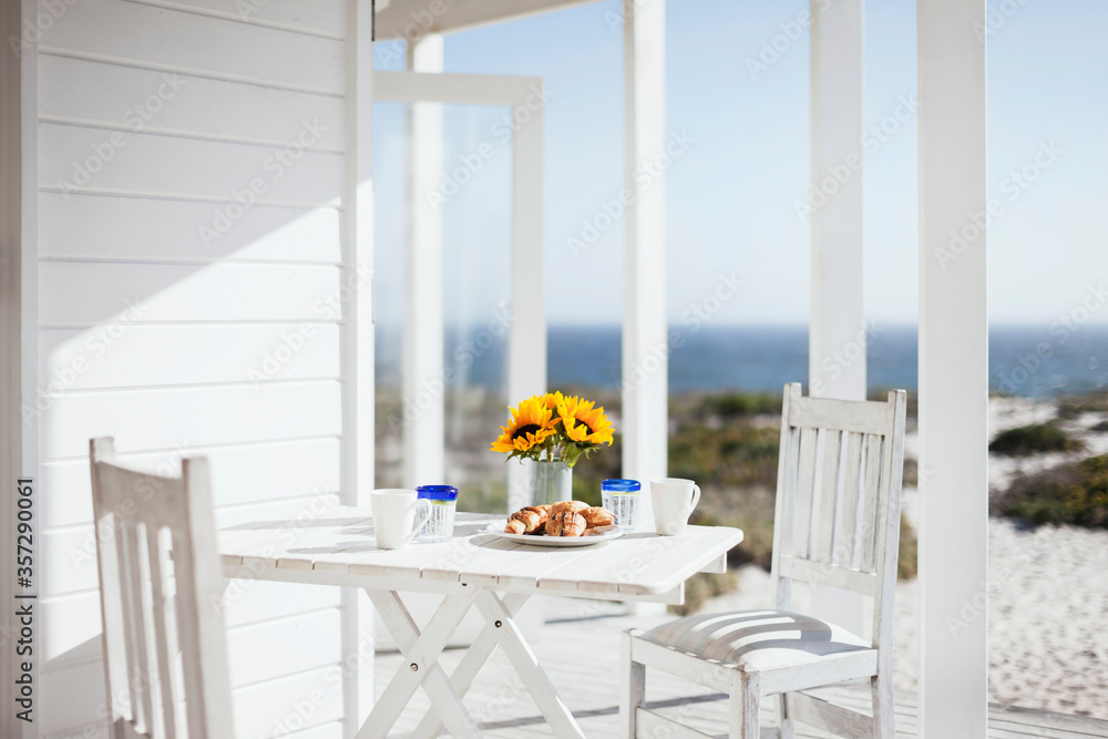 Vase of flowers, coffee and pastries on patio table overlooking ocean