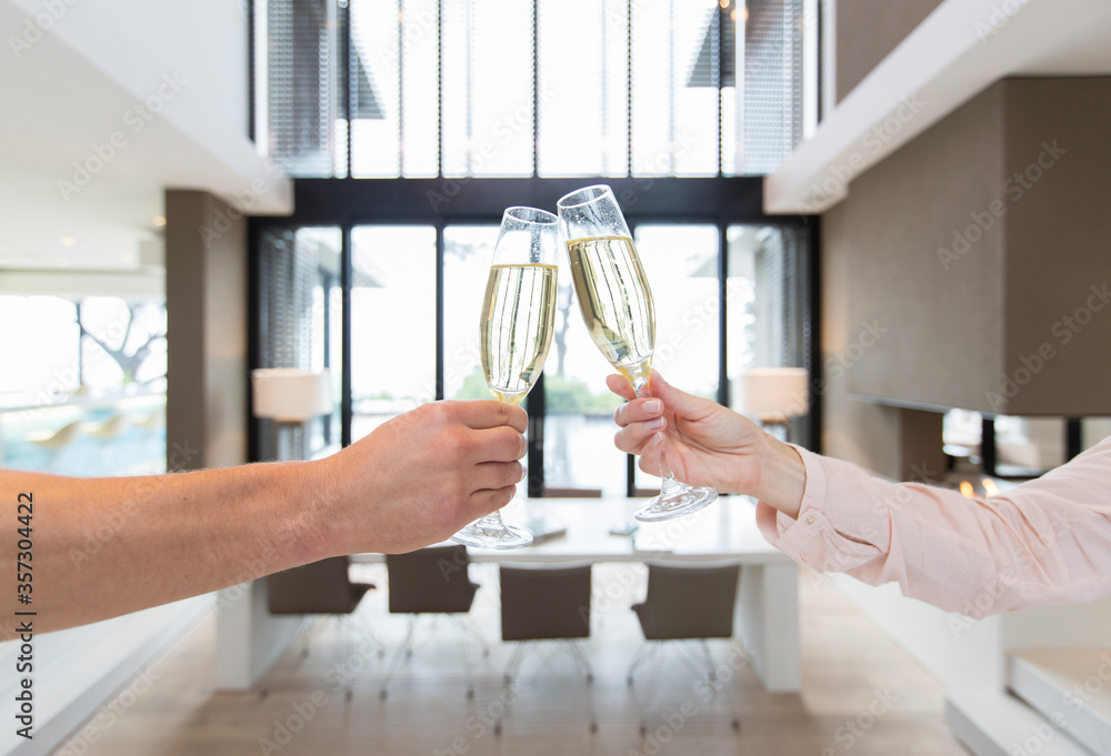 Hands of couple raising toast champagne flutes in modern dining room