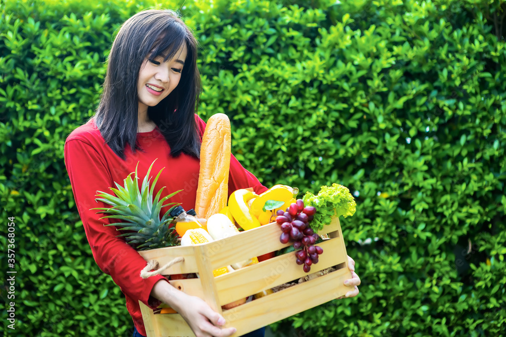 亚洲女人拿着装有蔬菜的木篮。篮子里有新鲜蔬菜。在花园野餐
