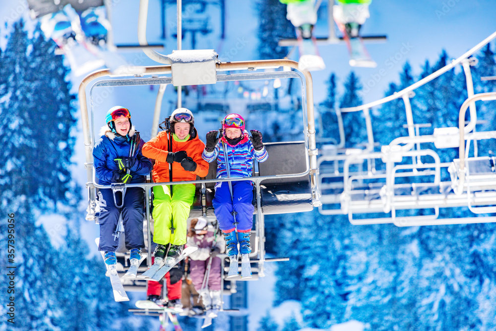 Three girls in colorful outfit sit on the ski lift talking and smiling together lifting on top of th