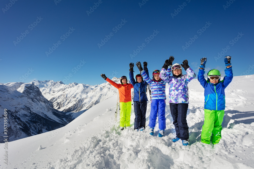 一大群滑雪孩子站在雪上，双手愉快地微笑着越过c山脉的山峰