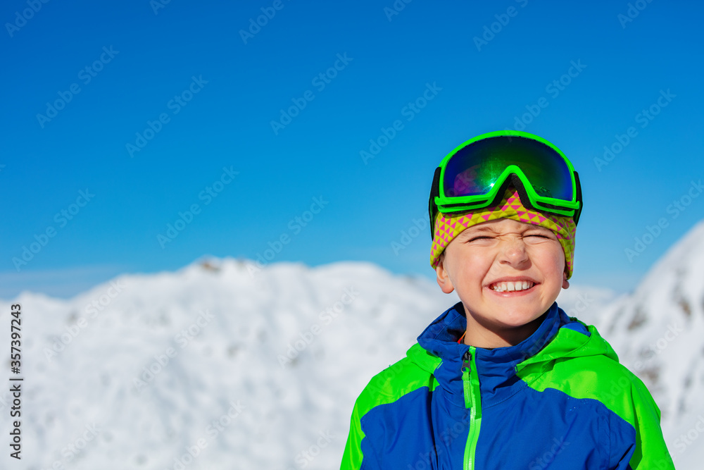 Close portrait of a boy in casual hat and ski or snowboard glasses over bright sunny mountain snow t
