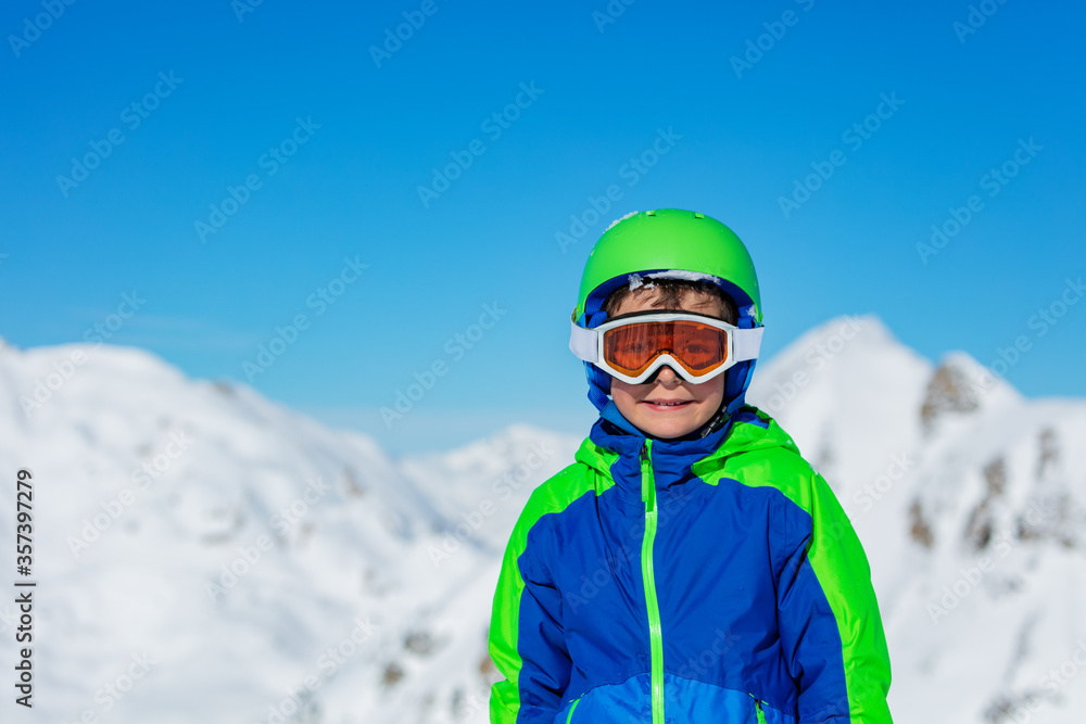 一个戴着运动头盔、戴着滑雪或单板滑雪眼镜的男孩在阳光明媚的山雪上的近景