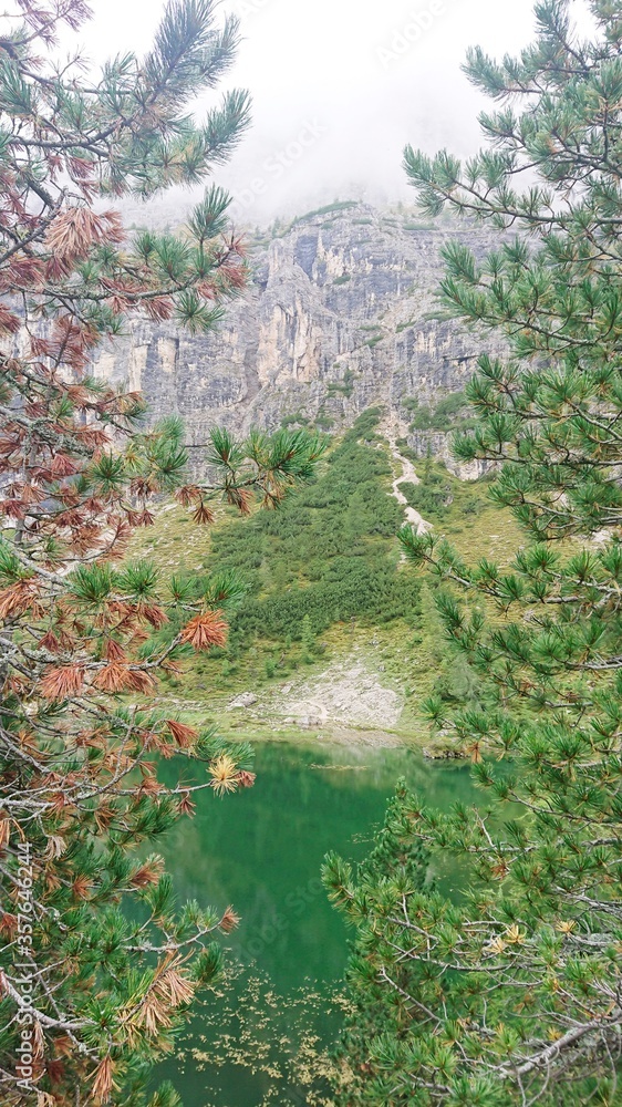 Bright summer landscape in the Dolomite mountains of Italy. The lake is green and two tall spruce tr