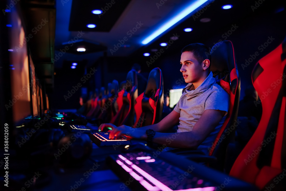 Focused young gamer playing video game at internet cafe, portrait.