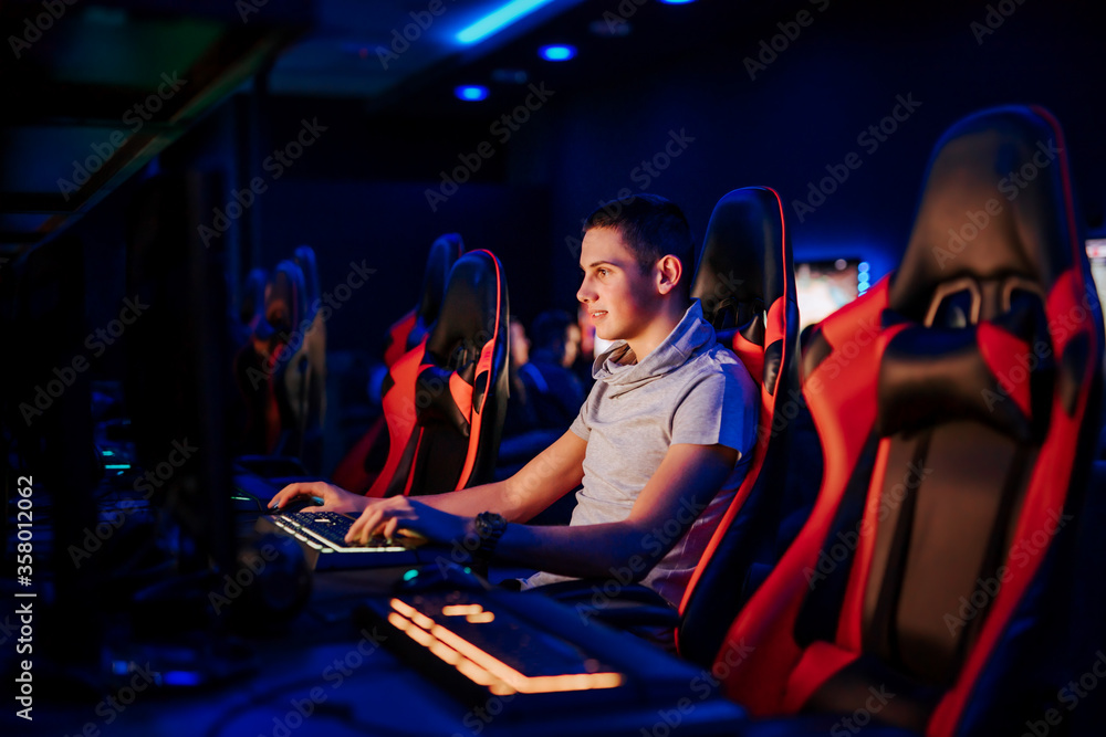 Smiling young professional gamer playing video game at internet cafe or playroom, portrait.
