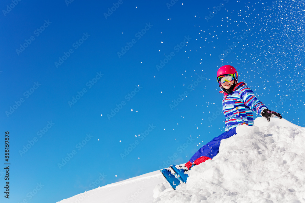 穿着五颜六色滑雪服的可爱漂亮女孩在蓝天上向空中扔雪