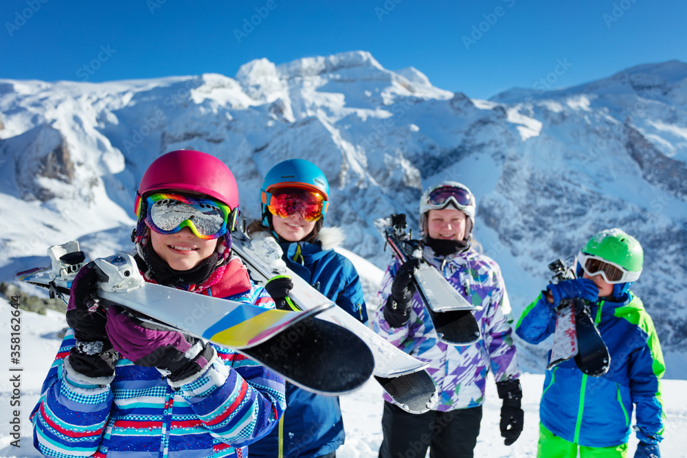 Portrait of a smiling cute girl in pink helmet and color googles hold ski in her hands in a group of