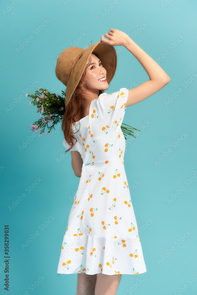 迷人的年轻女子，穿着夏装，戴着草帽，手里拿着雏菊花束，看着她的鞋子