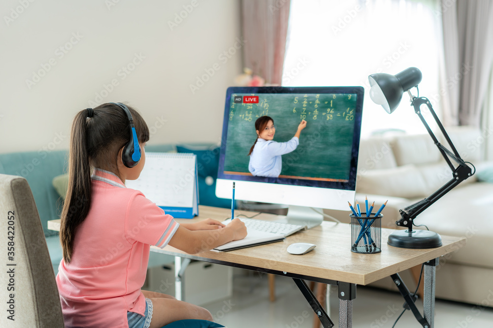 亚洲女学生与老师在家里客厅的电脑上进行视频会议电子学习。e-l