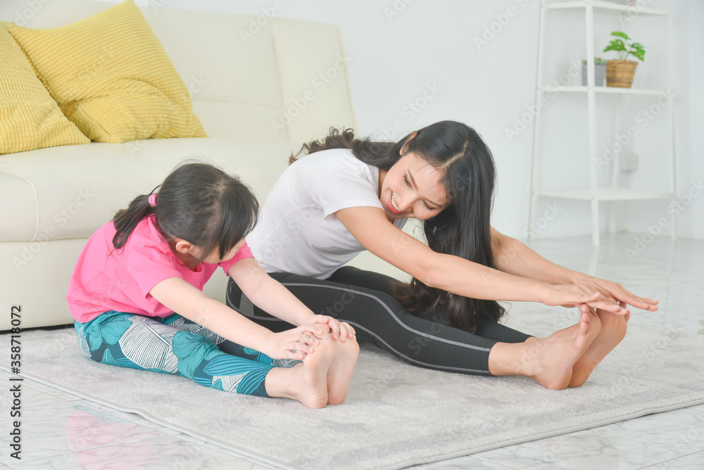 亚洲母亲和女儿在家一起练习瑜伽。母亲和孩子坐着伸展t