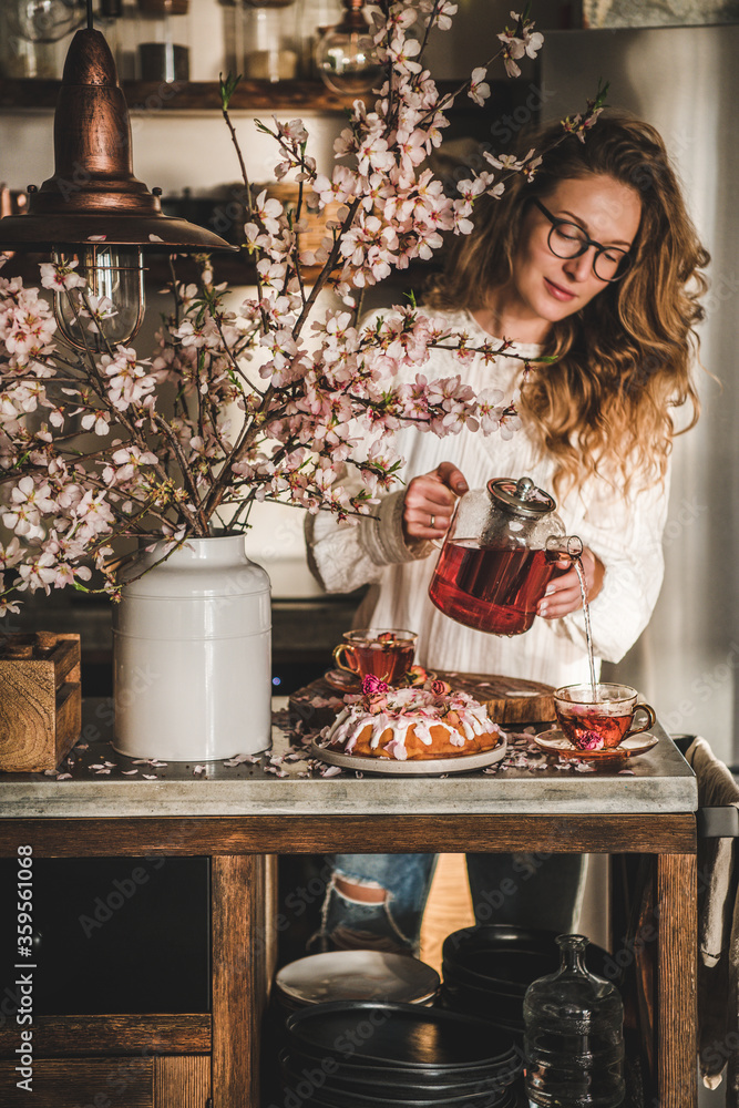 春天或夏天的茶和蛋糕。年轻的金发女人在混凝土厨房里把红茶倒在杯子里