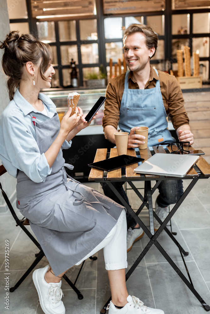 一对年轻的咖啡馆员工坐在桌子旁喝咖啡时进行了一些商务对话