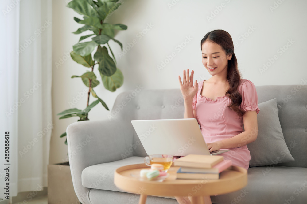 一名年轻的亚洲女子在客厅用笔记本电脑给她的朋友打电话。