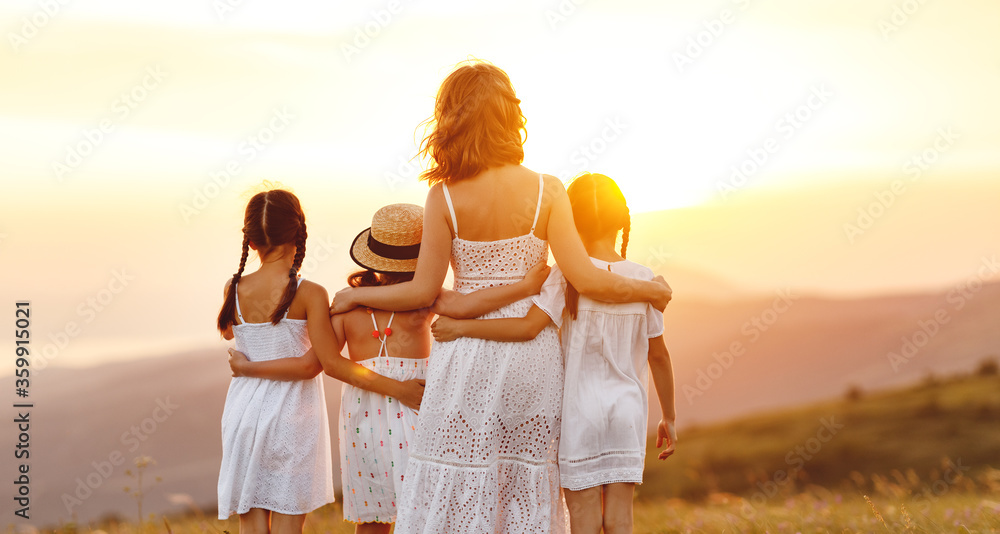 夏日户外快乐家庭。日落时分，母亲拥抱孩子和女儿。